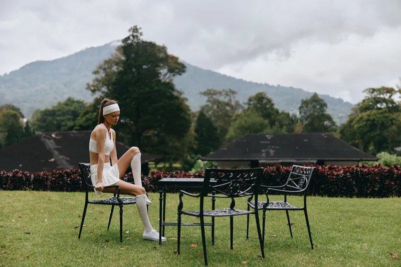 Young athletic woman posing in sporty white outfit on a green lawn with mountain view, showcasing fitness lifestyle and outdoor beauty