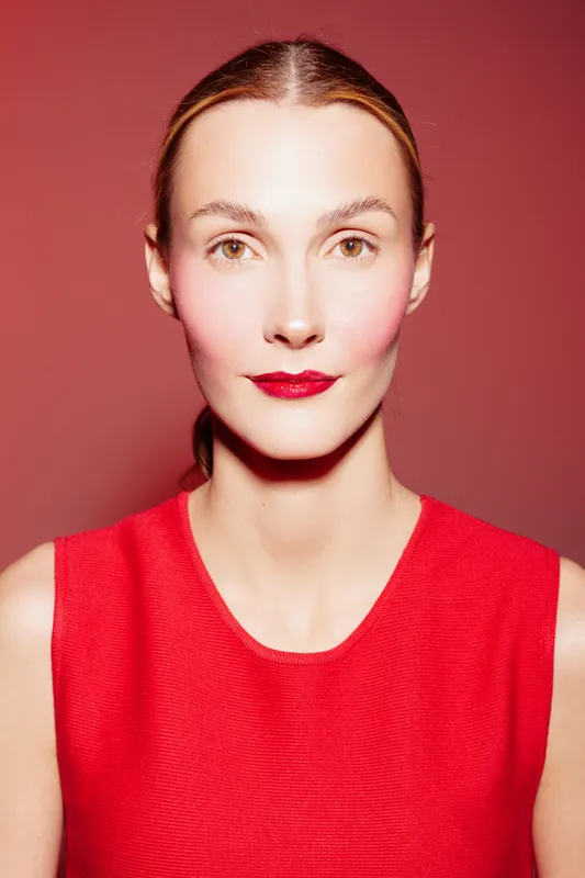 Portrait of a confident woman with red lipstick and red sleeveless top against a red background. Concept of beauty, fashion, and bold makeup style in studio lighting.