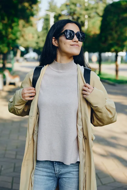 Woman outdoors fashion sunglasses jacket backpack park casual confident street style captured in a sunlit park, highlighting relaxed urban lifestyle and chic apparel