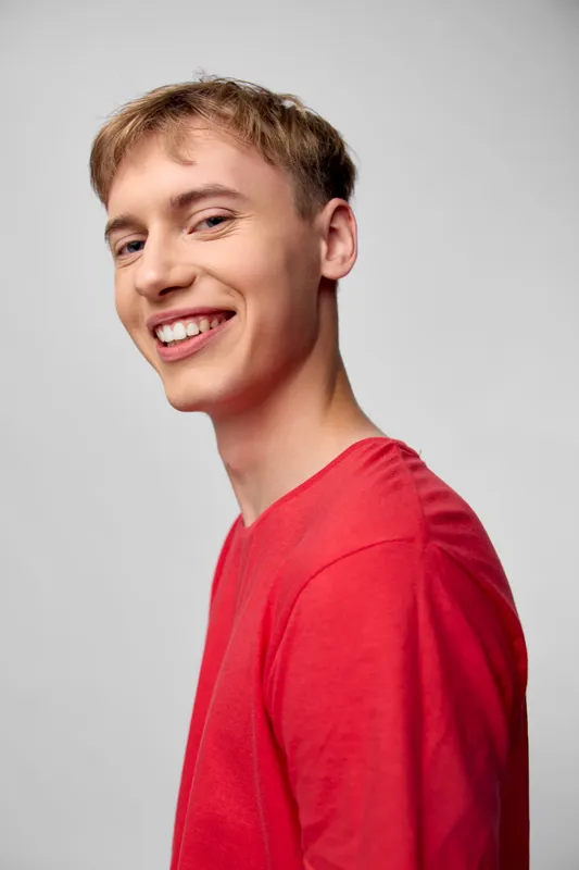 Man with a bright smile wearing a red shirt in a clean studio, casual mood and warm lighting, projecting approachable, friendly energy for lifestyle and fashion campaigns