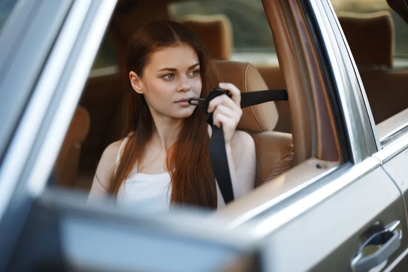 Young woman in a car looking contemplative while holding a seatbelt, reflecting on life's journey, showcasing a serene emotion and soft color tones.