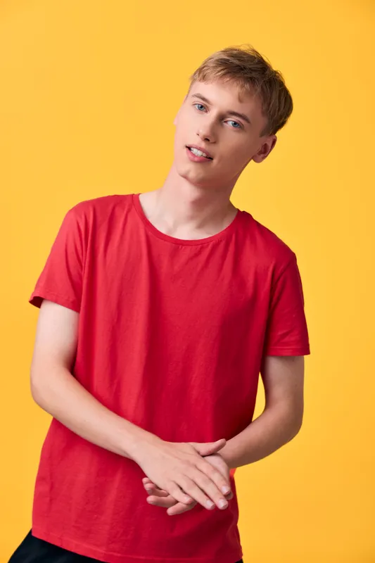 Young man in a red shirt stands against a vibrant yellow background, showcasing casual style, relaxed pose, and bright mood suitable for fashion, lifestyle, or product visuals.