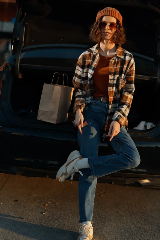 Woman by car trunk with shopping bags, casual outfit, sunglasses and beanie in golden hour glow, authenticity and candid lifestyle mood, mindful living and emotional storytelling.