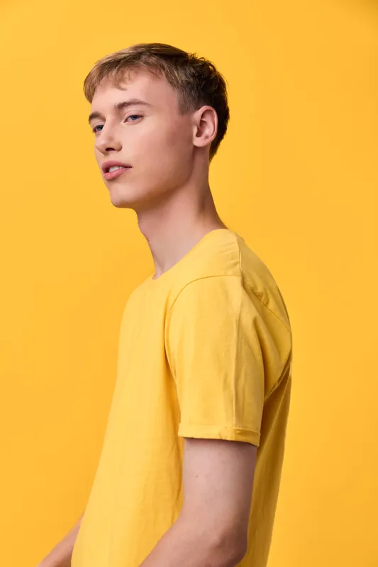 Young male in a bright yellow tee against a vibrant yellow backdrop, casual fashion mood, clean studio lighting, simple composition, modern style, fashion shoot, warm color palette, relaxed pose