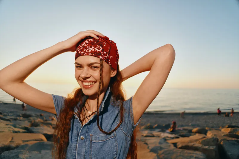 smiling woman in modern boho-western denim street style wearing a red bandana outdoors at sunset with warm film color tones