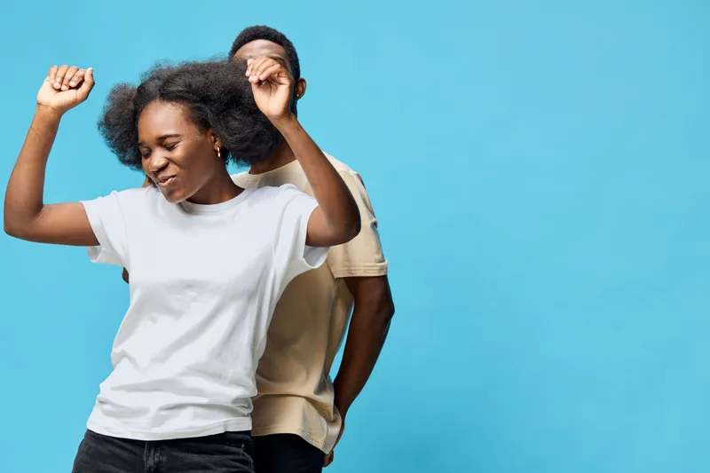 Joyful young African couple dancing together against a bright blue background, expressing happiness and love in a stylish and modern setting