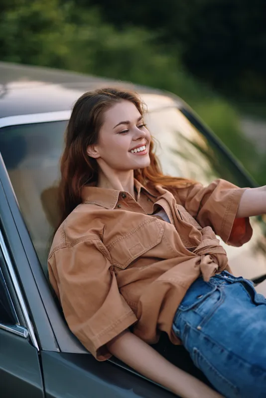 Young woman enjoying a sunny day, smiling and relaxing in a casual outfit, embodying happiness and freedom in a natural green setting.