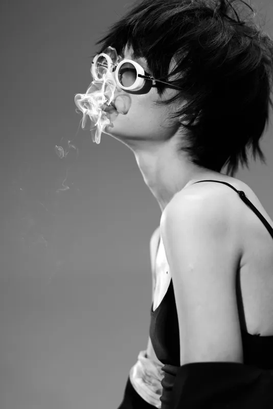 Black and white portrait of a young woman with short hair wearing goggles blowing smoke in artistic style