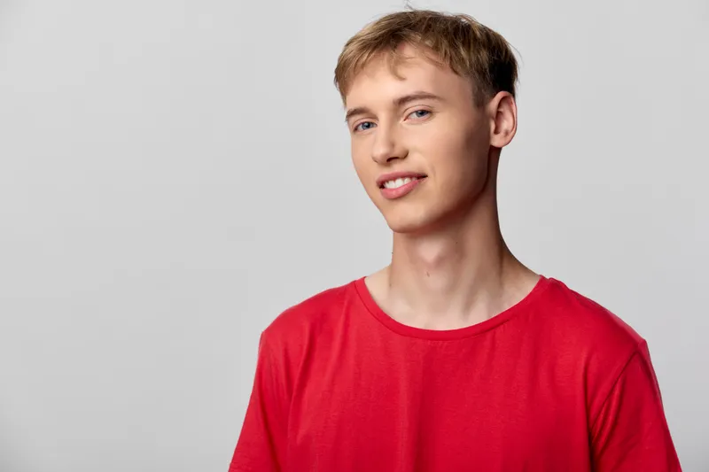 Man in a red tshirt stands in a bright studio with a relaxed smile, showcasing casual fashion, clean background, and crisp lighting for lifestyle or ecommerce imagery