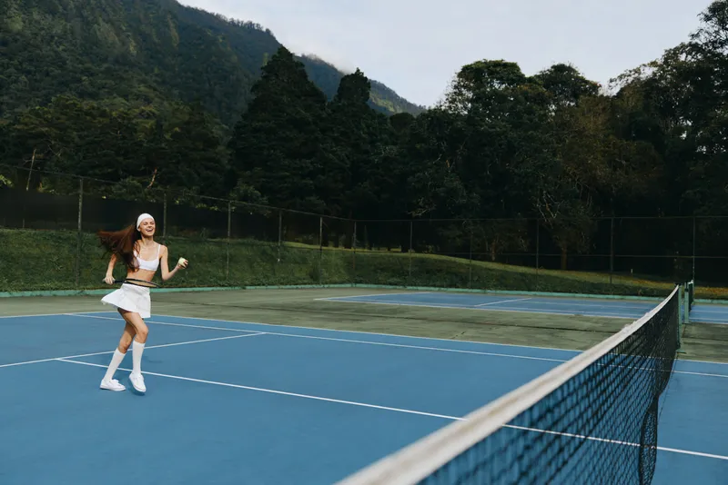 Energetic young female tennis player enjoying a match on a sunny day, showcasing athletic wear and vibrant emotions on a picturesque outdoor court