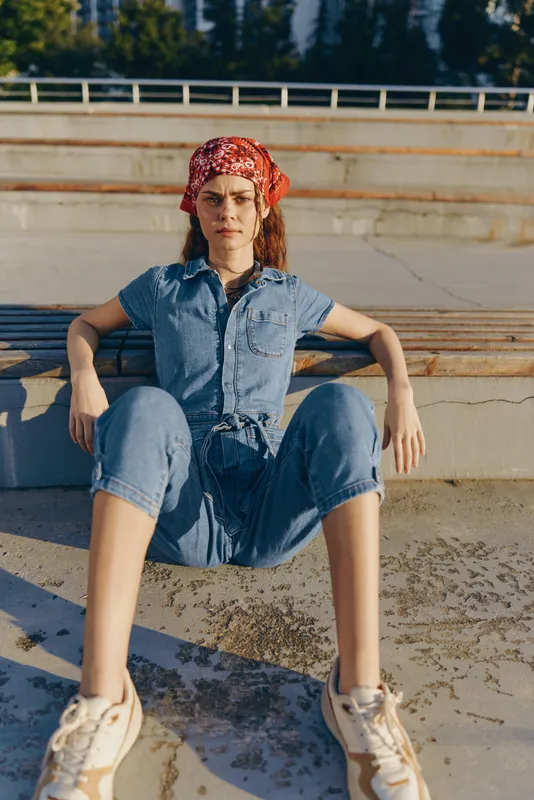 Modern boho-western denim street style woman relaxing outdoors in casual outfit with red bandana and sneakers, film color capturing natural sunlight and urban vibe.