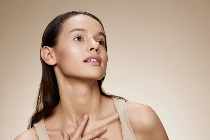 Elegant woman with natural makeup showcasing a serene expression against a warm neutral background, representing beauty and confidence in a minimalist style