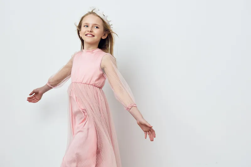 Joyful girl in a delicate pink dress, spinning with happiness, showcasing innocence and playfulness against a soft white background