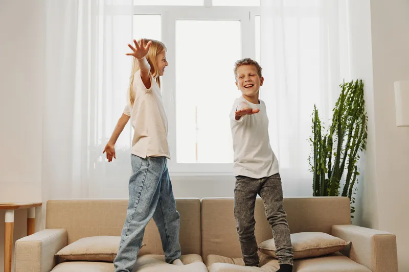 Happy children standing on couch in bright living room playing and laughing, enjoying carefree moment together. Concept of childhood joy, family fun, and indoor activity at home.