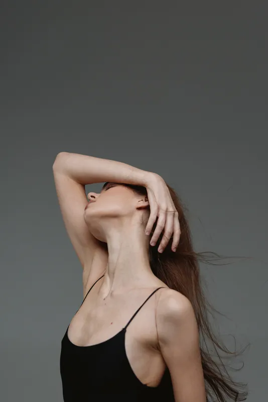 Elegant woman in black top posing with raised arm, minimalistic style, neutral background, graceful posture.