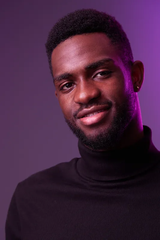Portrait of a smiling African male model in a black turtleneck against a purple background, showcasing confidence and modern fashion