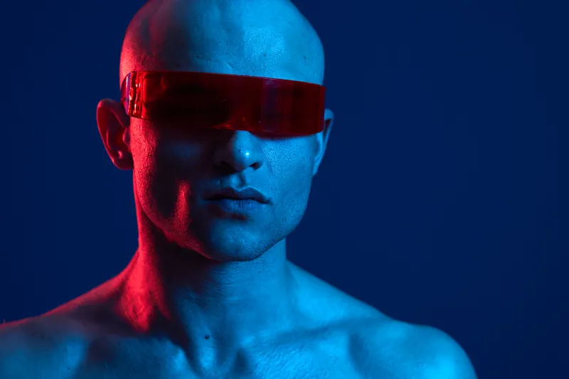 A striking portrait of a man with futuristic red glasses, showcasing an artistic blend of blue and red lighting, creating an edgy ambiance. Captivating and unique.