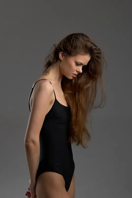 thoughtful woman in black bodysuit with long hair against gray background