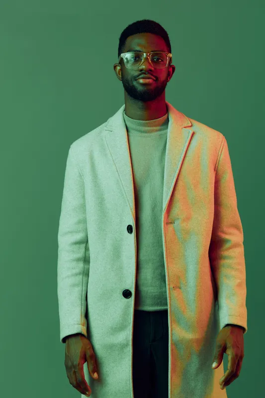 Stylish African man in a modern light gray coat against a vibrant green background, exuding confidence and sophistication, ideal for fashion related themes
