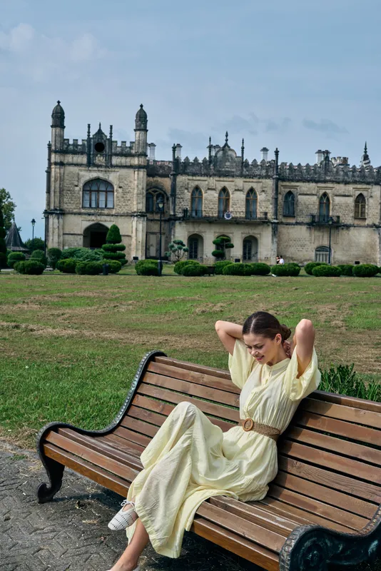 woman bench historic architecture dress park relaxation heritage authenticity inclusivity serene outdoor portrait of a smiling woman on a wooden bench on green lawn with backdrop