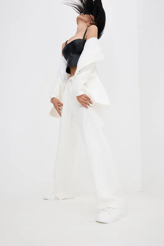Woman in white wide pants and black top posing in bright studio, dynamic movement with hair flipping, modern fashion style, minimalistic background lighting.