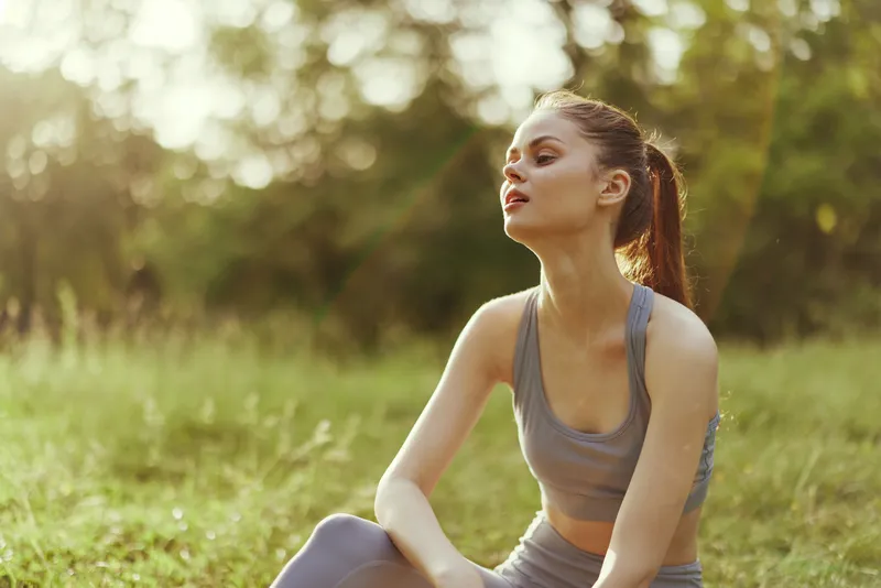 Young athletic woman in comfortable workout attire enjoying a moment of relaxation outdoors in a serene green park during sunset