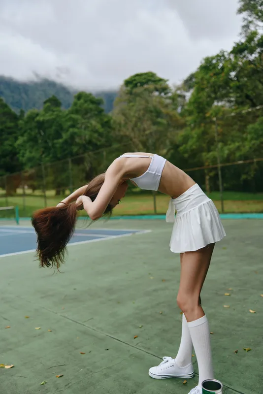 Young model practicing stretching exercises outdoors in athletic wear, showcasing flexibility and focus against a natural green backdrop