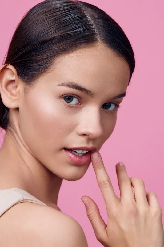 Young woman with mesmerizing gaze and finger on lips on a pink background, embodying beauty, confidence, and elegance in a fashion forward style