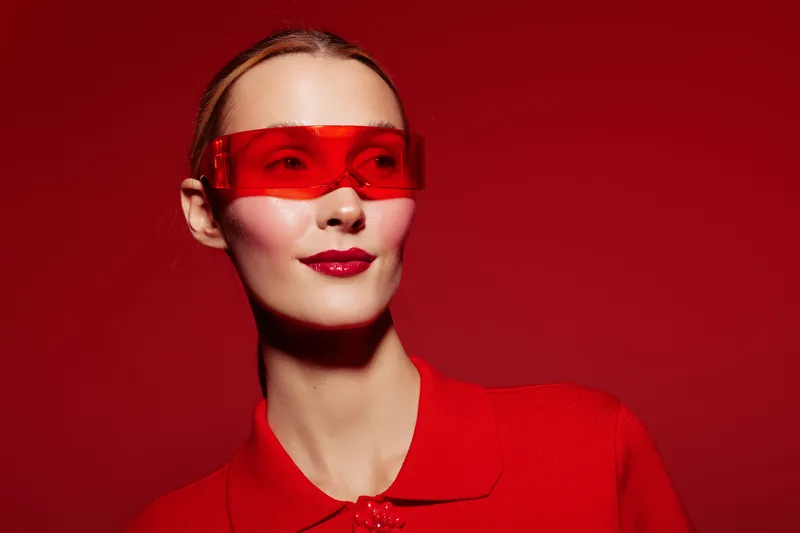 Young woman in red shirt and red sunglasses poses confidently on red background. Studio portrait with vibrant colors and modern fashion style. Concept of boldness and style.