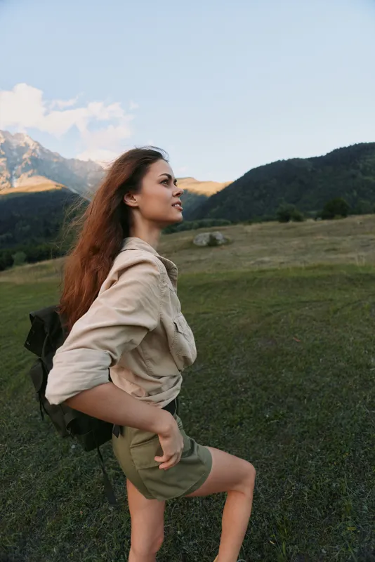 Woman with backpack hiking in a scenic field near mountains, embracing nature with a casual outfit, a serene outdoor lifestyle portrait capturing adventure and freedom, outdoorsy mood
