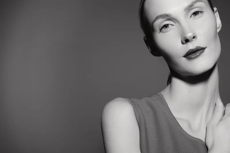 Portrait of a slender Caucasian woman with pale skin and slicked back hair posing against a dark background. Concept of elegance, beauty, and minimalism in studio lighting.