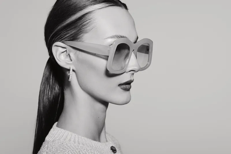 Profile of a young white woman with pale skin wearing oversized square sunglasses and a textured sweater. Studio portrait in black and white with minimalistic style and fashion concept.