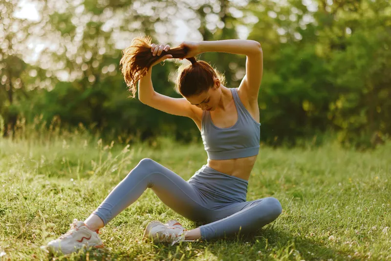 Fit young woman stretching outdoors in a serene green environment, wearing activewear, showcasing a healthy lifestyle and positive emotions during her workout