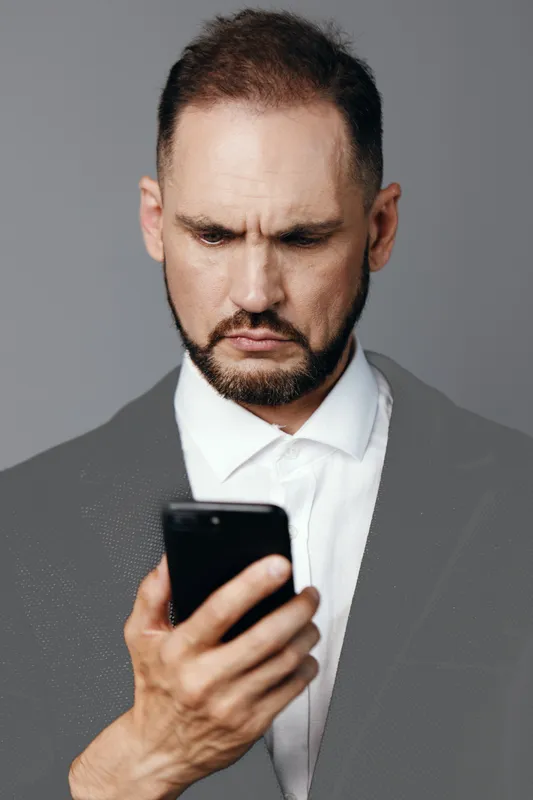 A focused business professional man studies a smartphone against an isolated colored backdrop, conveying calm focus, determination, and curiosity for corporate and leadership themes.