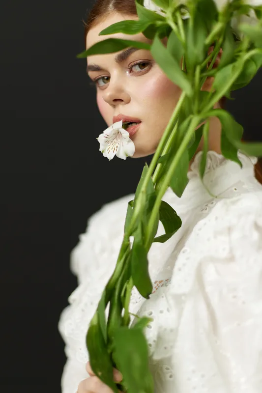 Young woman in elegant white dress holding a flower, showcasing beauty, nature, and grace against a dark backdrop