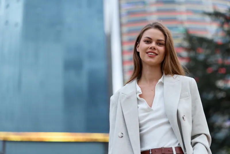 confident woman in beige blazer smiling outdoors urban business portrait with modern city background and stylish outfit