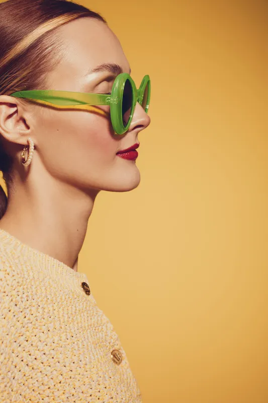 Profile of a stylish woman wearing green sunglasses and red lipstick against a yellow background. Concept of fashion, summer style, and confident female portrait.