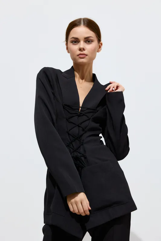 fashion woman posing in stylish black outfit with lace-up detail, neutral expression, minimalistic white background, modern and chic look