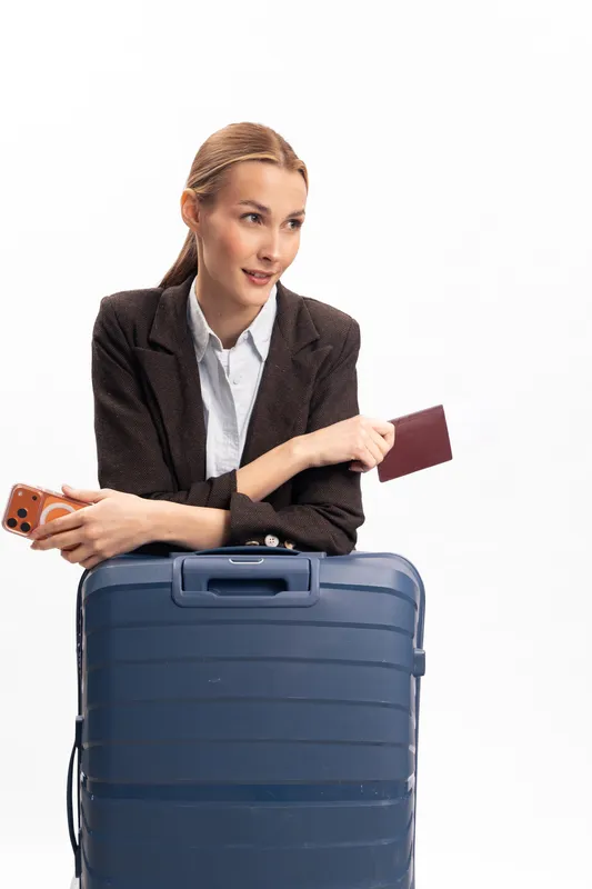Young woman in formal jacket holding passport and phone leans on blue suitcase. Concept for travel, business trip, and vacation planning with modern lifestyle and tourism.