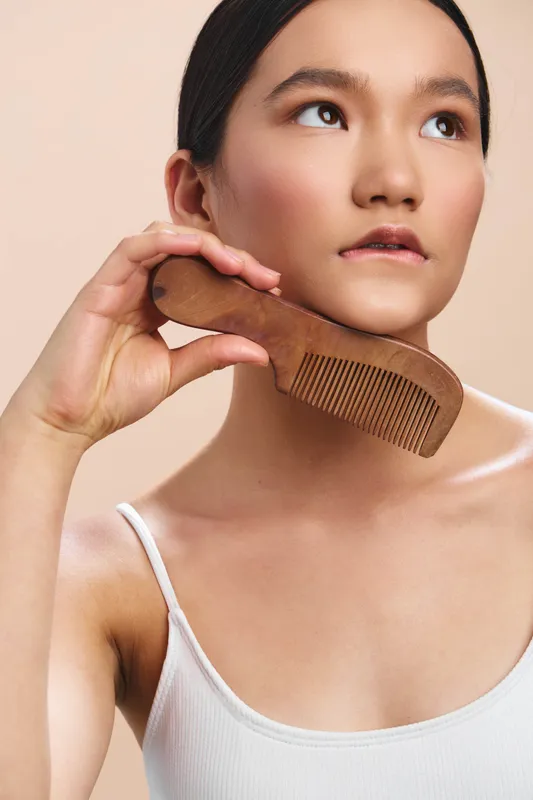 asian woman with a wide wooden comb in a soft studio setting, engaging in a gentle grooming moment that highlights selfcare, beauty routine, and calm personal care.