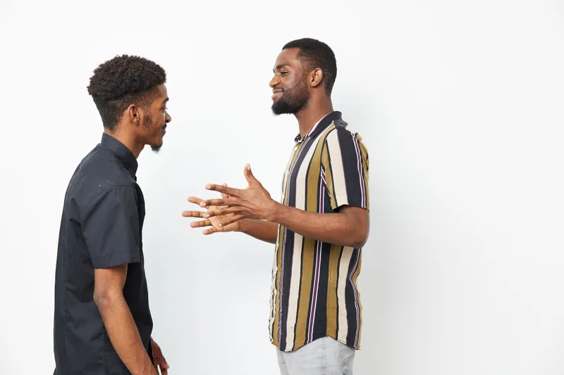 A lively scene featuring two black men engaged in conversation, showcasing friendly expressions and dynamic body language. Ideal for themes of communication and connection.