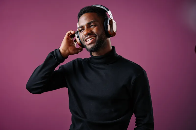 Happy young Black man enjoying music with headphones on a purple background, showcasing modern style and vibrant emotions