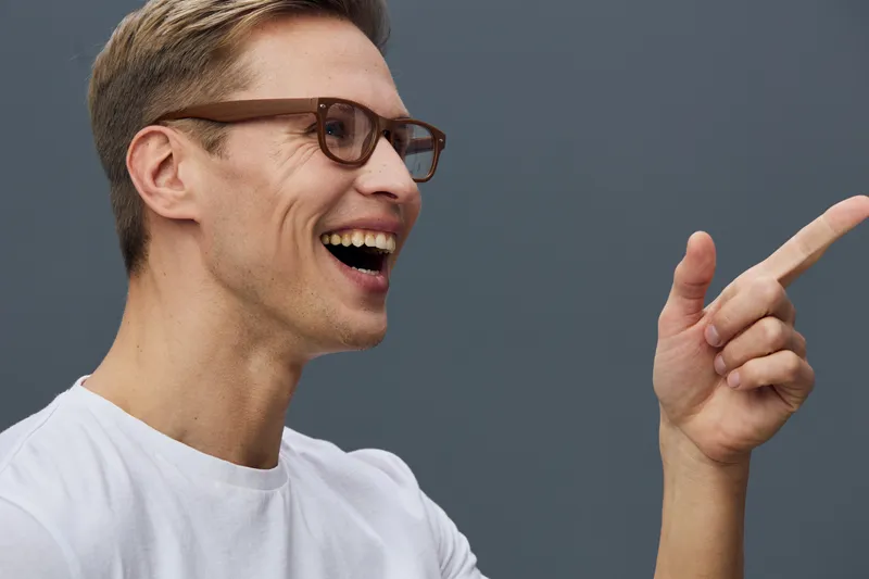 Smiling man with brown hair and glasses wearing casual white t-shirt gesturing with his hand isolated on plain gray background, studio portrait with cheerful mood and friendly expression. People lifes
