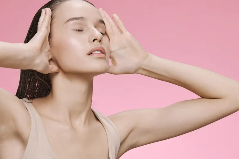 Young woman with closed eyes expressing tranquility against a soft pink background, showcasing beauty and serenity through minimalistic styling