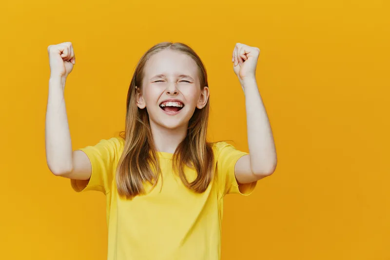 Happy girl celebrating success against a bright yellow background, showcasing joy and excitement in a casual summer outfit