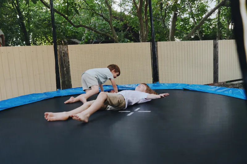Two joyful children playing on a trampoline, showcasing laughter and fun in a lush green backyard setting. Perfect for capturing moments of childhood happiness.