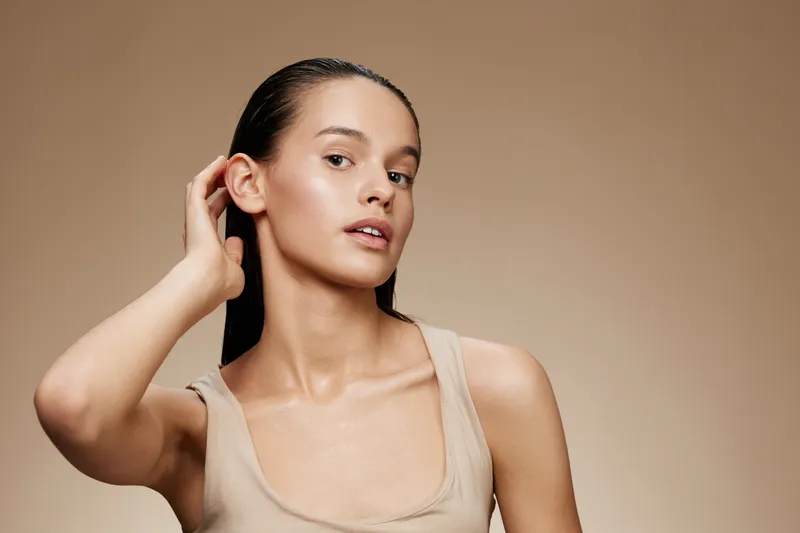 Natural beauty portrait of a young woman with long dark hair in a beige top against a soft brown background, conveying calmness and elegance
