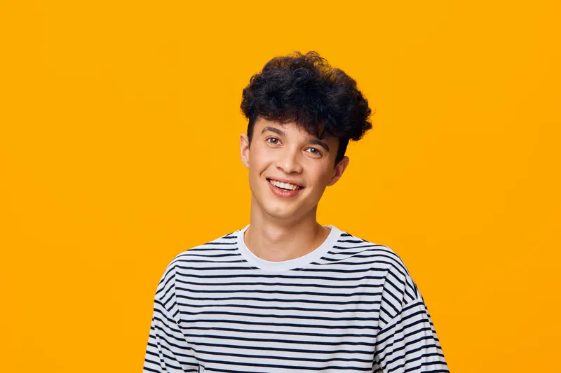 smiling man with curly hair wearing striped shirt on vibrant orange background, cheerful expression and casual style, bright studio portrait