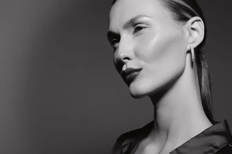 Portrait of a young caucasian woman with light skin and sleek hair in black and white. Elegant look with earrings and subtle makeup in studio.