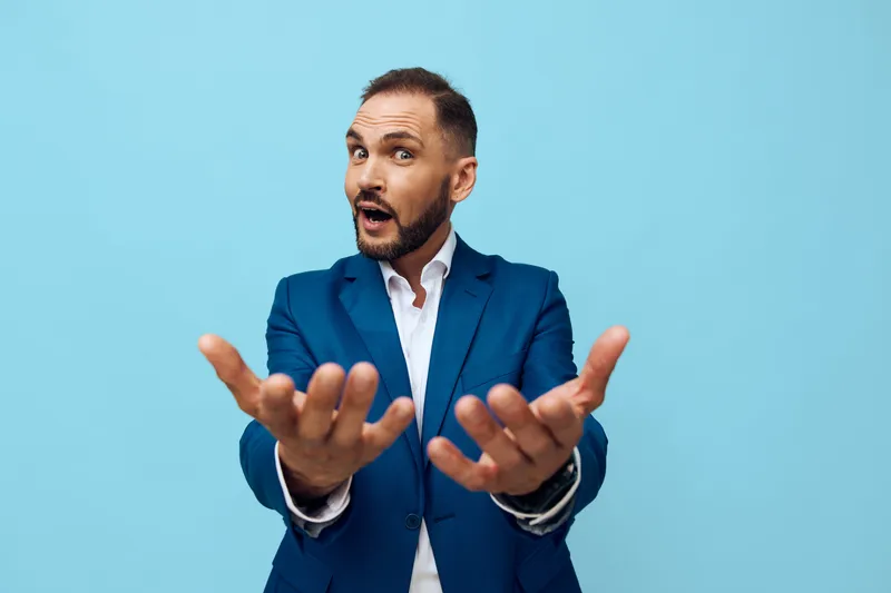A professional man in a blue suit on an isolated colored background, displaying business focus with open hands and a curious expression, inviting engagement and confident communication.